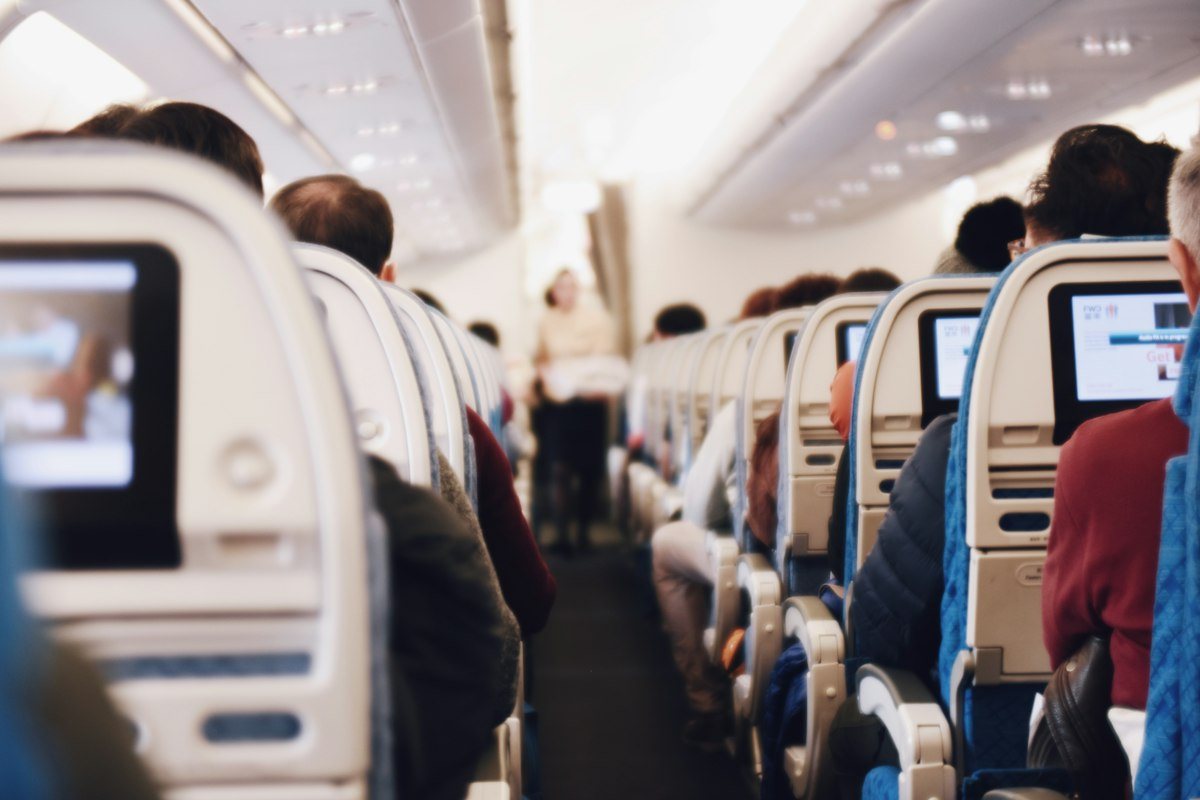 The aisle of a passenger plane with travelers seated and seat-back screens on