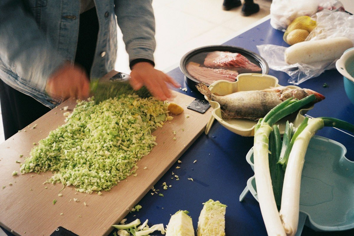 A cook chopping fresh greens on a cutting board surrounded by vegetables
